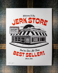 An 8"x10" white art print featuring a black-and-red illustrated storefront with the text 'Welcome To The Jerk Store' and 'You're Our All-Time Best Seller!', a reference to a quote by Jason Alexander's character George Costanza in the NBC sitcom Seinfield, placed on a plaid fabric background. Other details in the print include typography reading 'Shrimp Cocktail Served all day!' and Believe it or not, we're open!