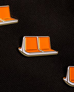 Three enamel pins shaped like classic NYC orange MTA subway seats with white sides and gold metal outlines pinned to a black canvas background