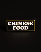 Chinese Food restaurant sign enamel pin with 'CHINESE FOOD' text in white on a black background and gold metal border