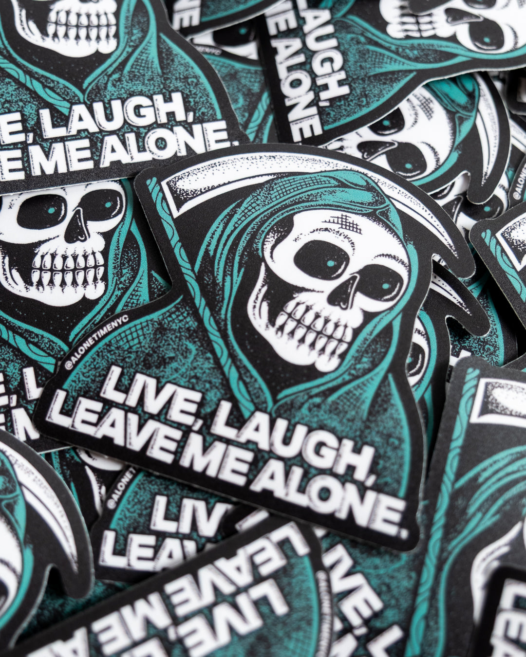 A pile of die-cut stickers featuring a heavily stippled illustration of a grim reaper skull in a green hood, holding a sickle, with the text 'LIVE, LAUGH, LEAVE ME ALONE.' 